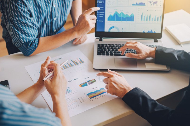 Dwie osoby dyskutujące nad wynikami biznesowymi, analizujące raporty papierowe i wykresy na laptopie, ilustrujące zwrot z inwestycji w profesjonalną stronę wizerunkową stworzoną we Framer.